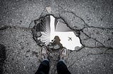 person looking at their reflection in a puddle