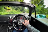 image of driving on the left in the UK. A sports car, and a convertible with greenery outside.