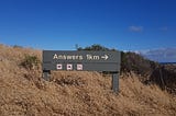 Trail sign with the message “Answers 1km” with an arrow pointing right