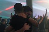 Two men with short dark hair hugging. They appear to be White.