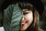 Beautiful woman smiling, covering half her face with a leaf.