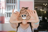 A woman faces the camera holding up a cookie in shape of a smiling poop emoji.
