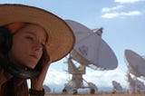Jodie Foster’s Ellie Arroway sits in front of the Arecebo Radio Telescope observatory in the film Contact, with headphones