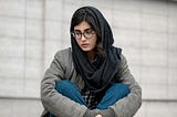 Brunette, Muslim female wearing dark grey hijab sitting cross-legged.