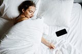 A Woman Sleeping Beside Her Smartphone. What happens when you track your sleep and run several experiments for a month to improve your recovery and sleep quality