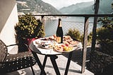 Countdown to my (2)5th Anniversary Celebration. Plates of food and wine on a small table. Balcony overlooking mountains and water.