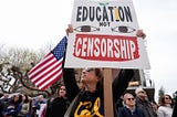 Protestors with a sign saying “Education not censorship” and an American flag