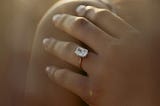 A woman wearing a diamond ring while holding onto her right shoulder with her left hand.