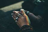 A woman clasps her hands in prayer. Silver rings adorn her fingers.