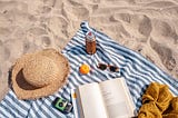 A beach towel with various items sitting on a beach.