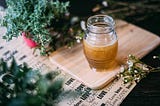 A jar of honey on a wooden board surrounded by greenery, symbolizing the richness of focus when spread thick, aligning with the metaphor of dedicating attention to fewer tasks for greater fulfillment.