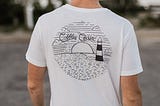 White t shirt with a black graphic on top. Picture of a subset and lighthouse