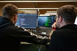 Two men looking at a monitor with code lines.