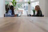 Two women with laptops facing each other at a conference room table.