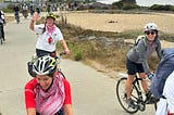 A view along the Bay Trail with three bicyclists from SURJ BA in front and many others following.