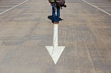 A man walking down a street with an arrow pointed backwards.