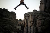 Girl jumping from one cliff to another. There is a large gap between the cliffs.