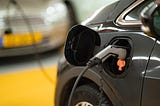 A picture of an electric car being charged. There is a grey charging nozzle sticking out of the charge port on the