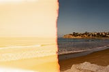 an old photo of a beach, stretching to the right, towards a town. The photo is faded and orange on the left half.