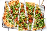 Slices of homemade pizza topped with tomatoes, vegetables, and leafy greens.