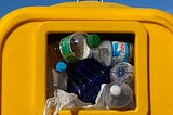 A bright yellow trash can filled with empty plastic bottles and plastic waste.