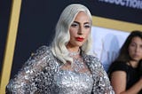 Lady Gaga, blond, on a red carpet, wearing a wonderful silver dress.