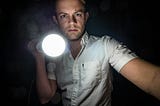 photo of a sinister looking young man shines a flashlight at the viewer — alt-text to boost accessibility