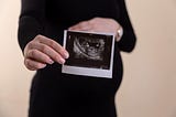 A photo of a pregnant woman holding a photo of her fetal ultrasound.