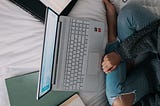 A girl is sitting on the bed and studing/learning/working.