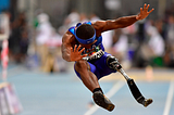 Paralympian male athlete jumping with head done and arms and legs out stretched — on leg is a prosthetic blade