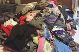 A mountain of clothes, mostly blacks, greys, and pinks, piled atop the author’s bed.