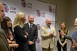 Six representatives from USAID stand with President Jimmy Carter. USAID employees smile and laugh as he makes a joke and spreads his arms out in front of him.
