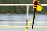 Person holding pickleball paddle and ball in front of net