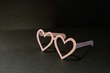 Pink heart shaped glasses on black background
