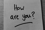 Black and white photo of a Post-it note with ‘How are you?’ written in black marker