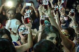 Women raise wine glasses and cheer, some masked.