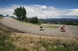 Two skateboarders on a downhill road at a hairpin turn