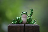 Figurine of a frog cheerily holding up the two-finger peace sign.