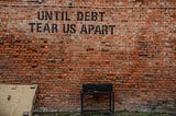 This is a picture of a brick wall with the words, “Until Debt Tear Us Apart” written on it.