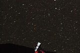 A white telescope on a red support stands before a starry night sky.