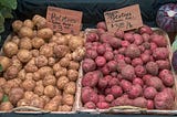 Two bins of potatoes, red and white, waiting to be roasted.