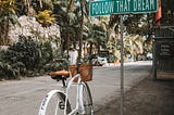 A cycle parked on a street near a sign saying Follow That Dream