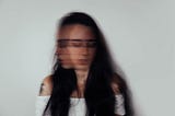 Blurry photo of a woman with black hair and a white shirt looking down and to the side.