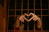 Hands reaching through a prison gate forming a heart