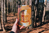 A photo of someone holding a copy of The Overstory in the woods.