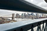 Brooklyn bridge and lower Manhattan seen from between a railing on Manhattan Bridge.