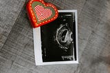 Red heart magnet pinning a black and white picture of an ultrasound with a new fetus