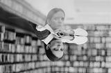 Grayscale photo of woman in a library with reflection