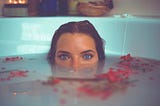 woman peeking out of the bath, which had petals on water surface
