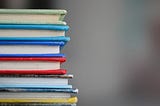 A stack of books — colored green, aquamarine, blue, red, grey and yellow.